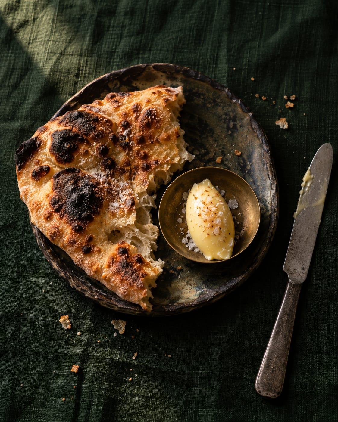 Torn wood-fired flatbread beside cultured butter with smoked salt